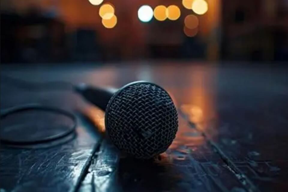 Photograph of a microphone lay on a wooden floor with twinkling lights in the background